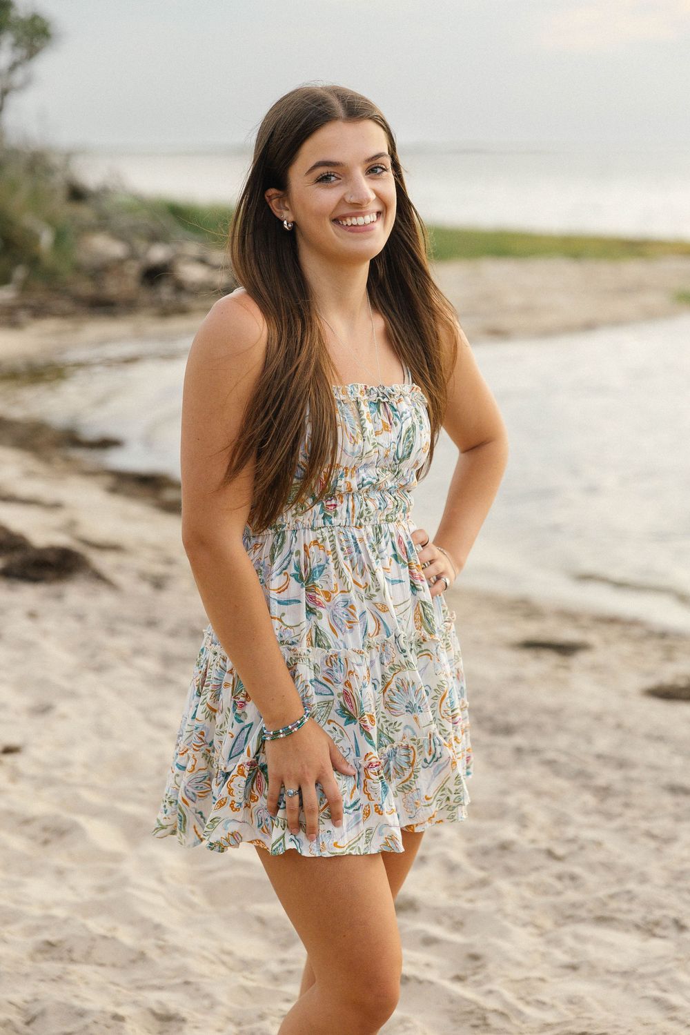 Woman in floral summer dress playing on sandy beach at sunset.