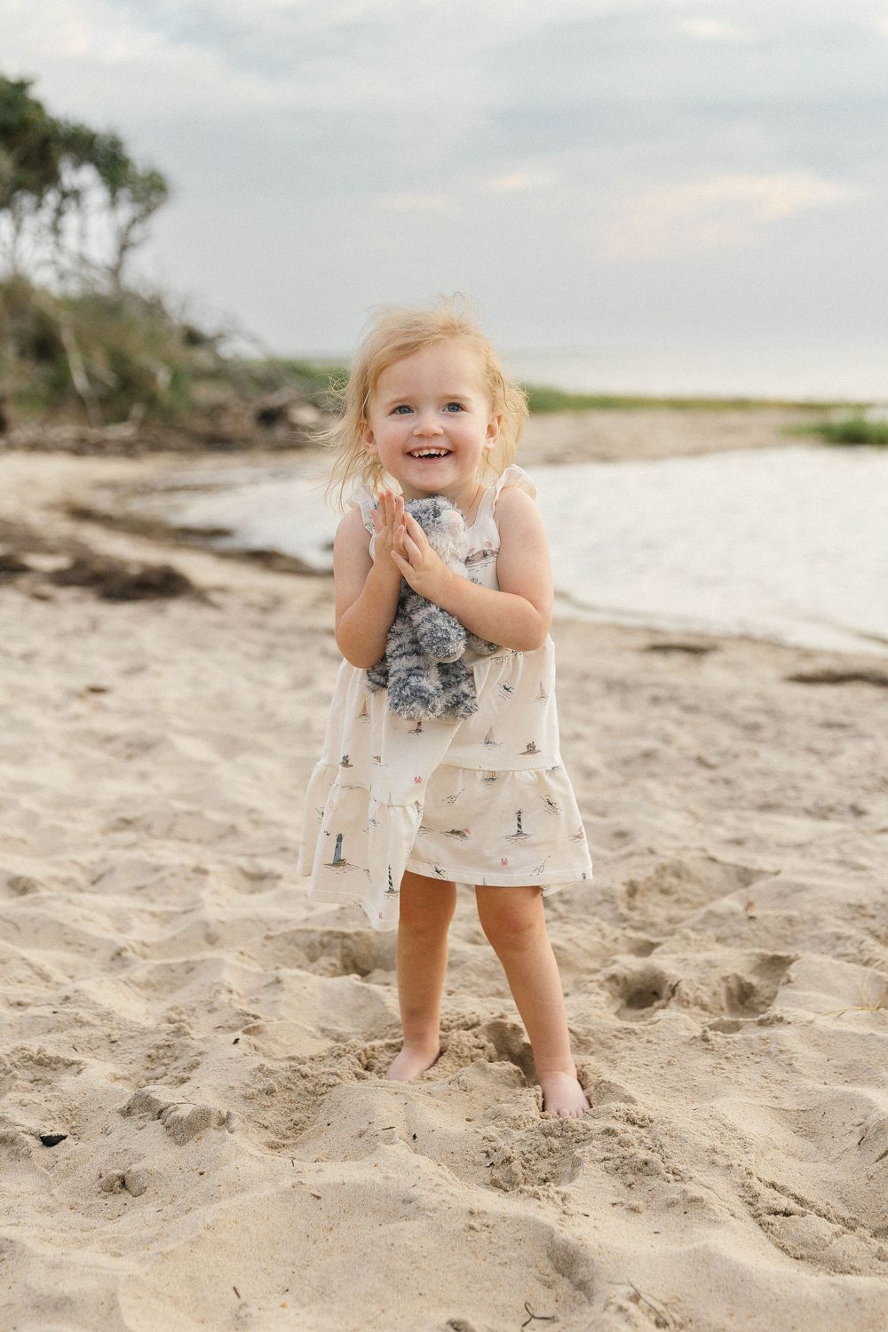 Young child playing and smiling on sandy beach near ocean.