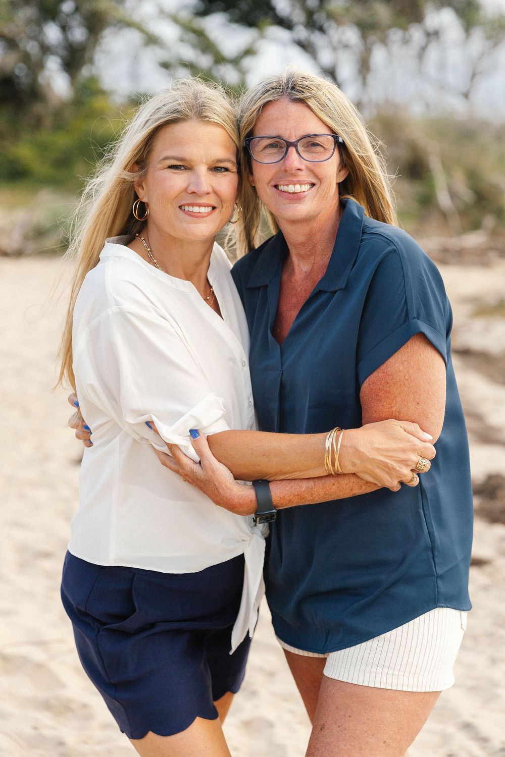 Two people embracing and laughing together on beach in coordinating navy and white outfits.