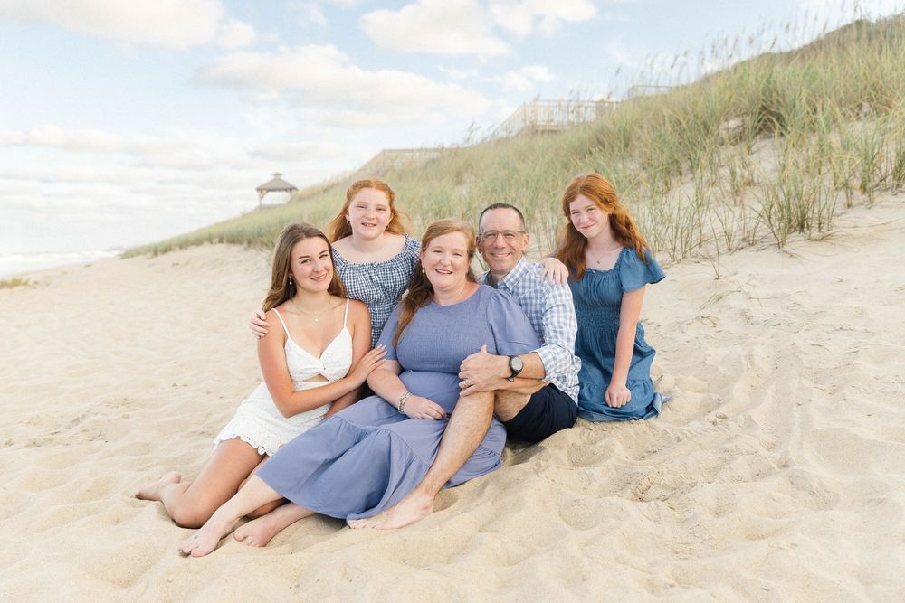 Family group lounges together on sandy beach dunes during sunset photo session.