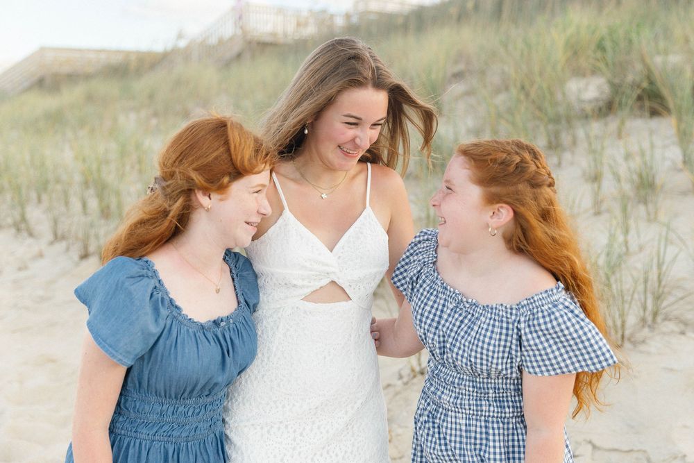 Group in coordinating blue and white outfits poses together on beach dunes.