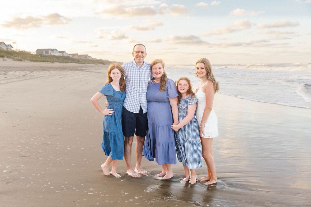 Family wearing coordinated blue and white outfits poses together on sunset beach.