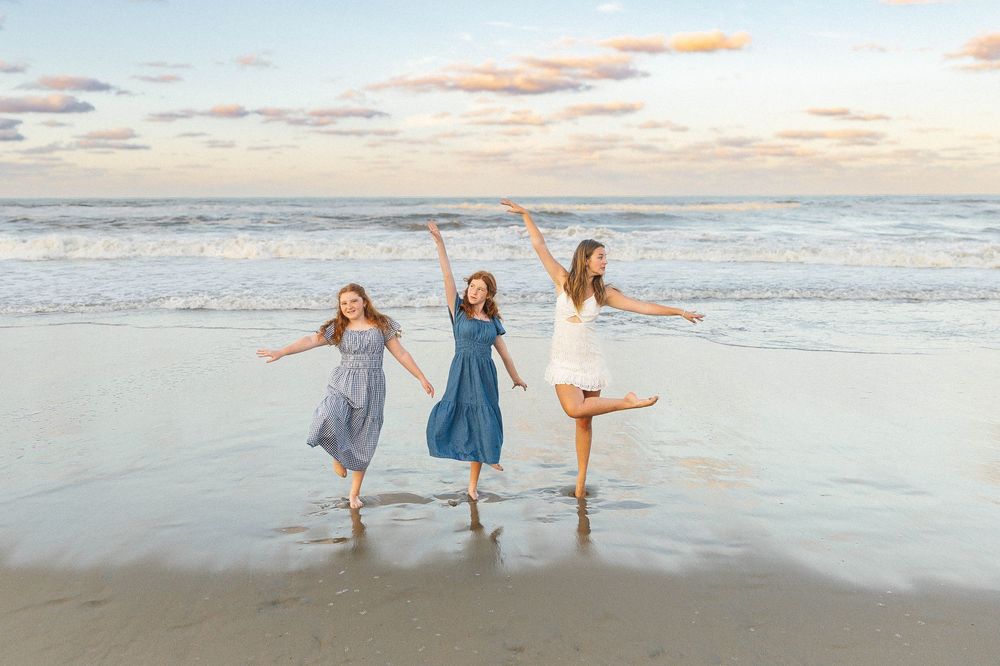 People playing and posing playfully at the ocean's edge during sunset.
