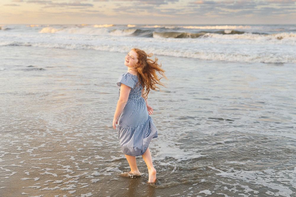 Ocean waves roll onto shore during golden hour as wind blows through beach grass.