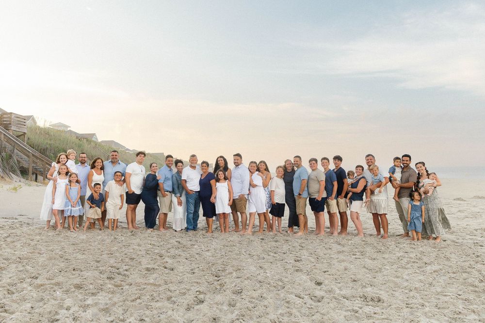 Large group photo of people in coordinated outfits on beach at sunset.
