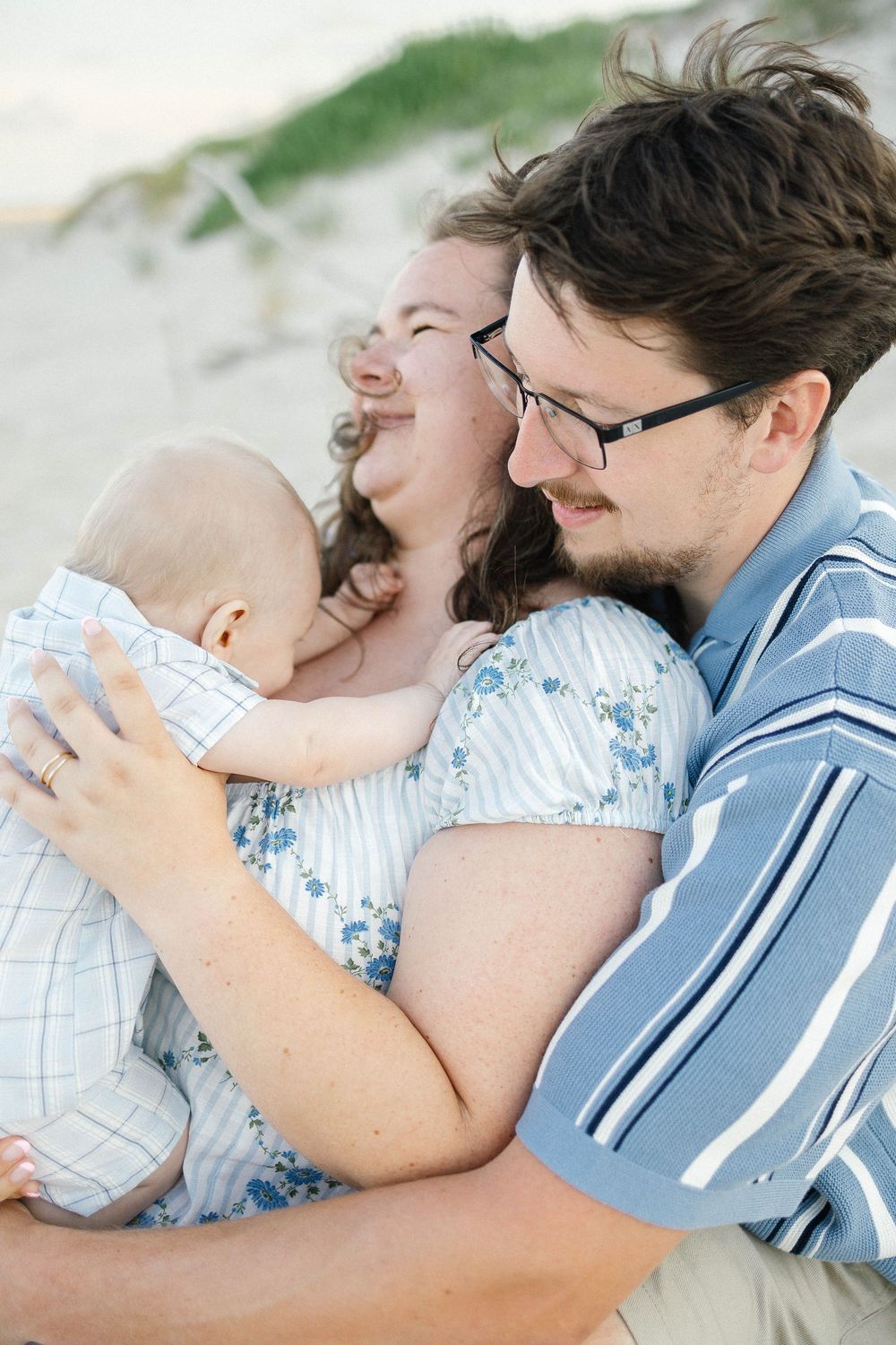 Happy young family with baby sharing a joyful moment together on a sandy beach.