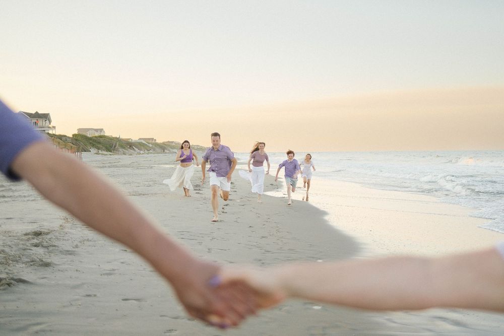 Family running on a sandy beach at sunset, with two people holding hands in the foreground.