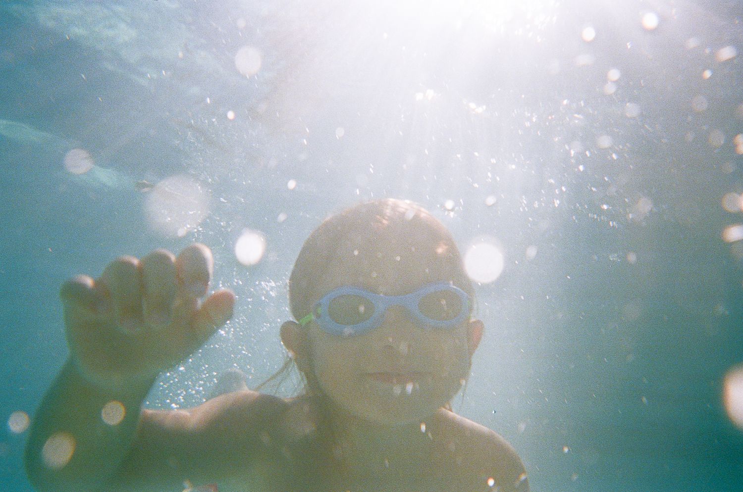 Underwater shot of a swimmer wearing goggles with bubbles and sunbeams in the pool.