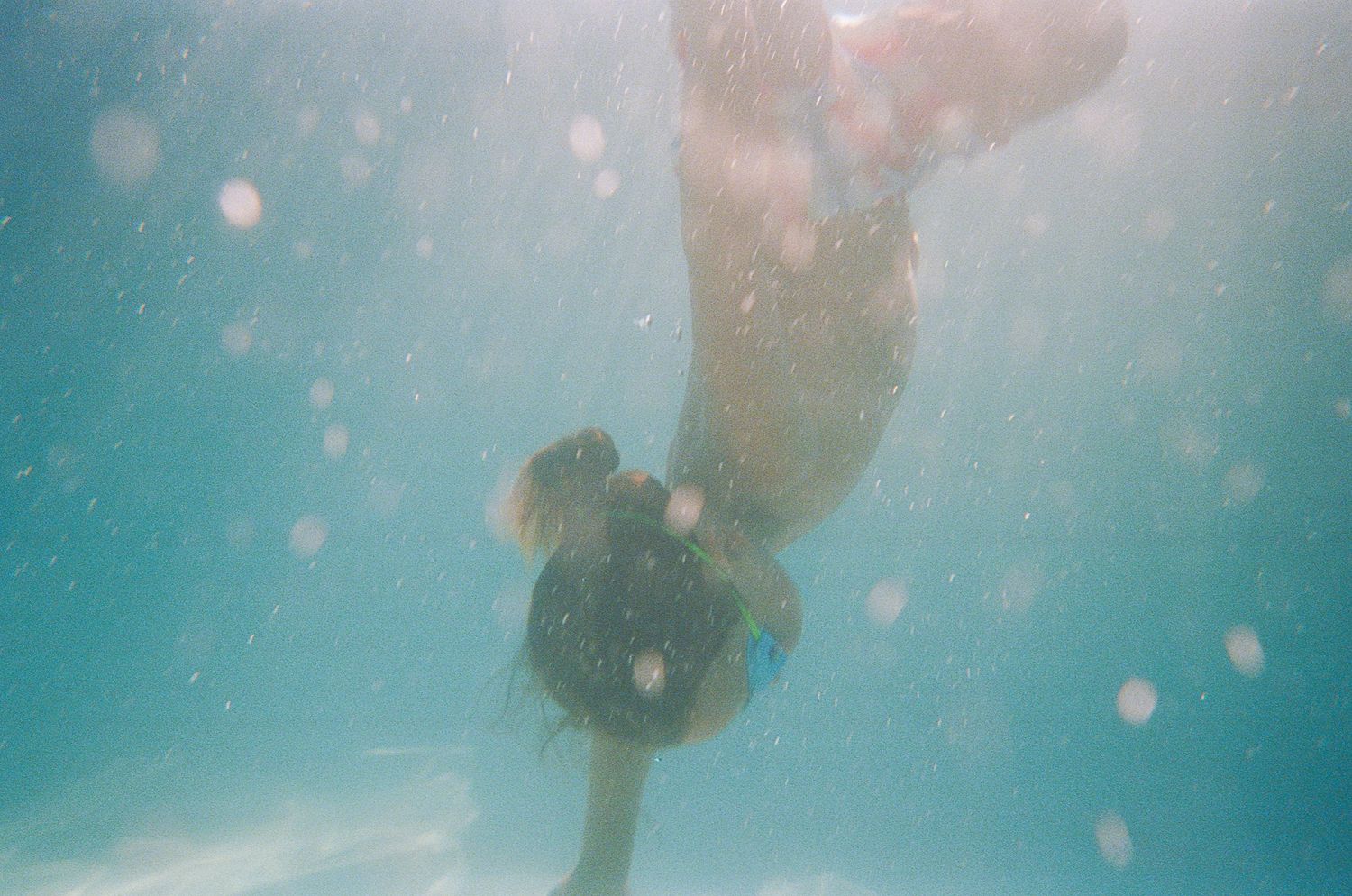 Underwater view of a swimmer diving with bubbles floating in turquoise water.