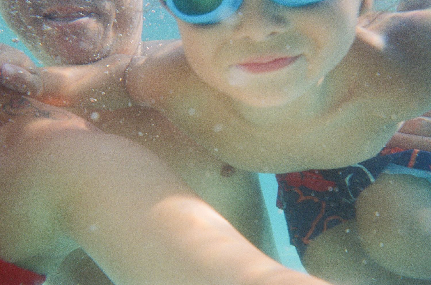 An underwater selfie showing swimmers with goggles in blue pool water.