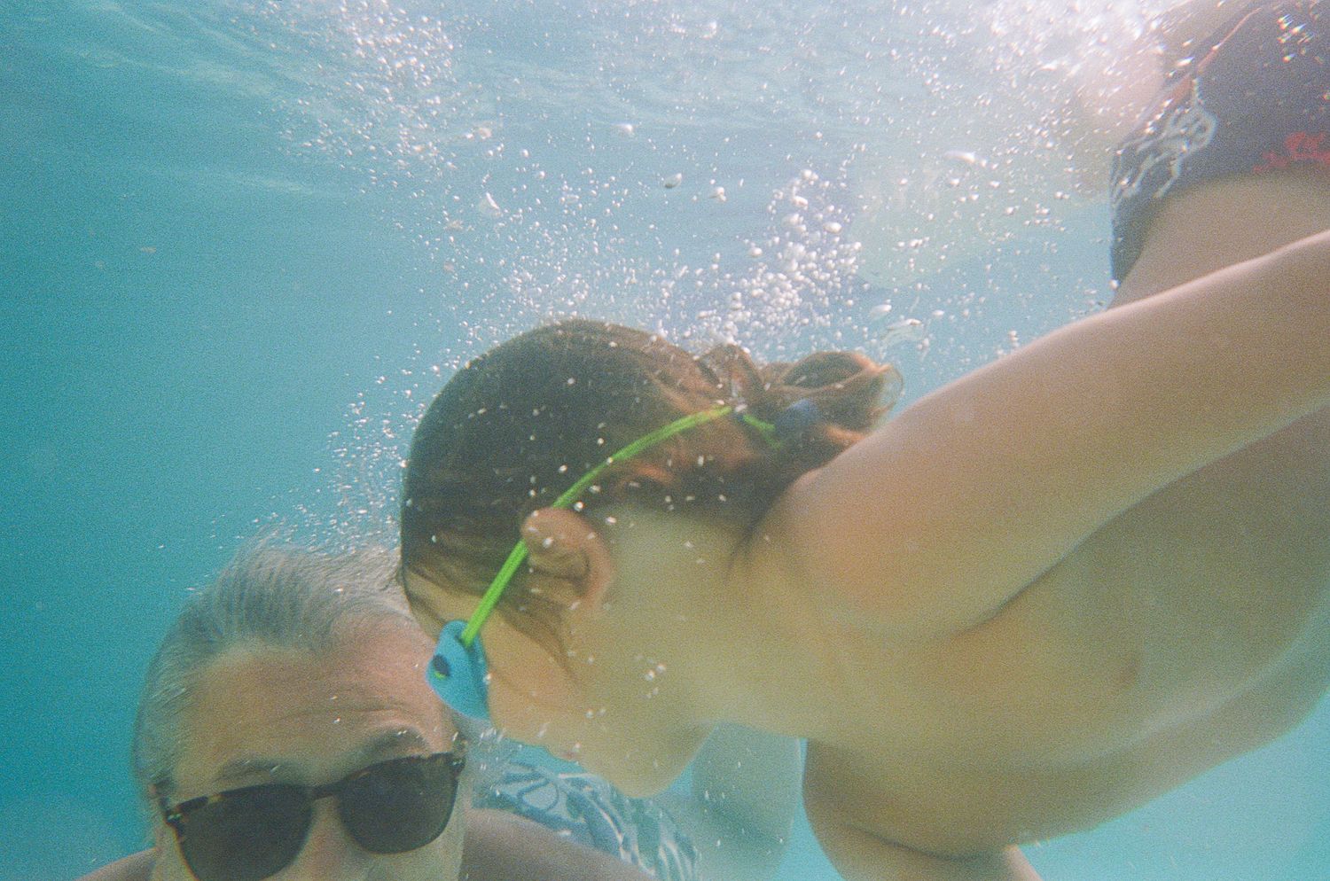 Two swimmers pose underwater in a pool with bubbles and turquoise water.