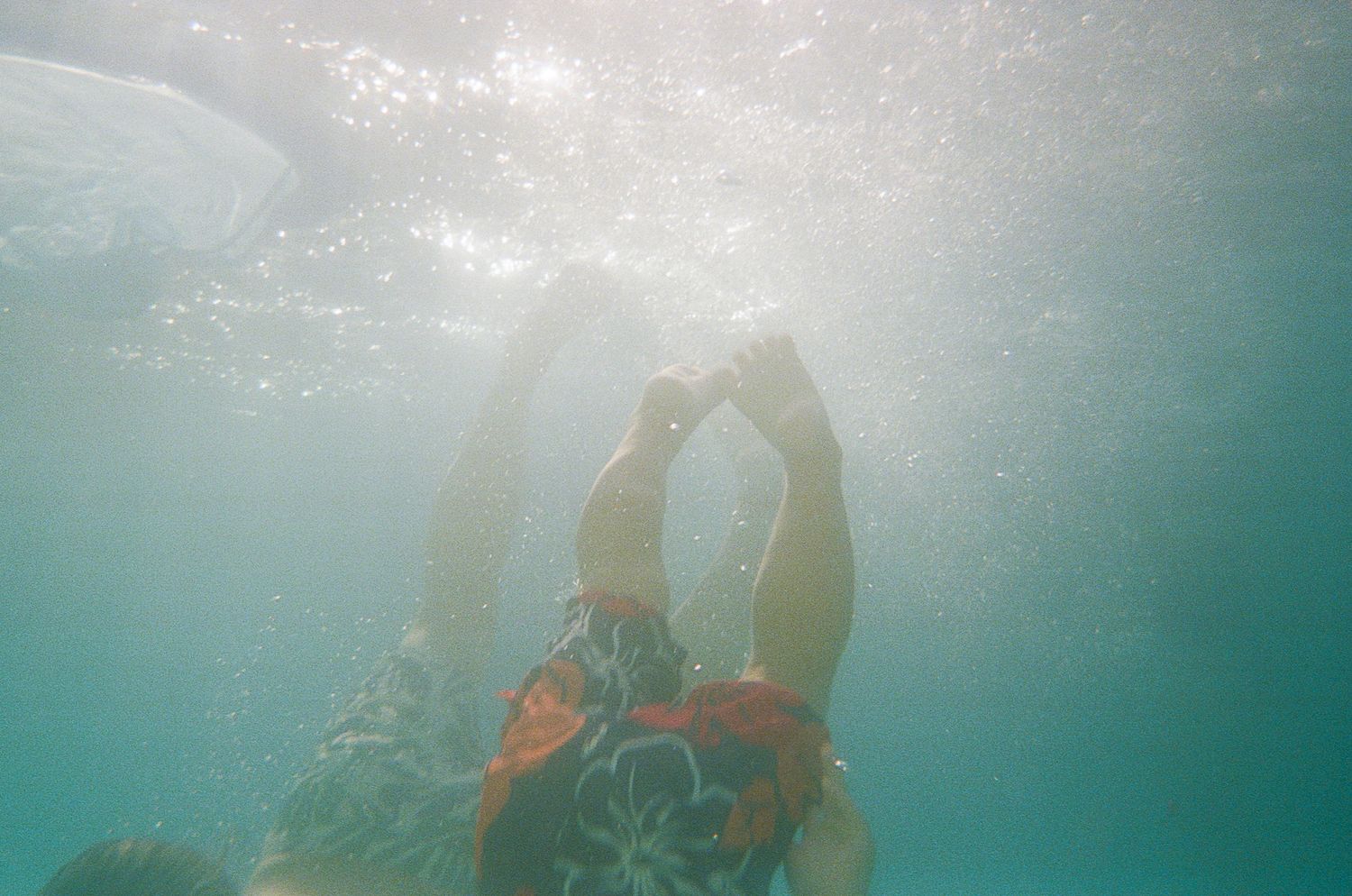 Underwater silhouette of a swimmer diving with sunlight streaming through the blue water.
