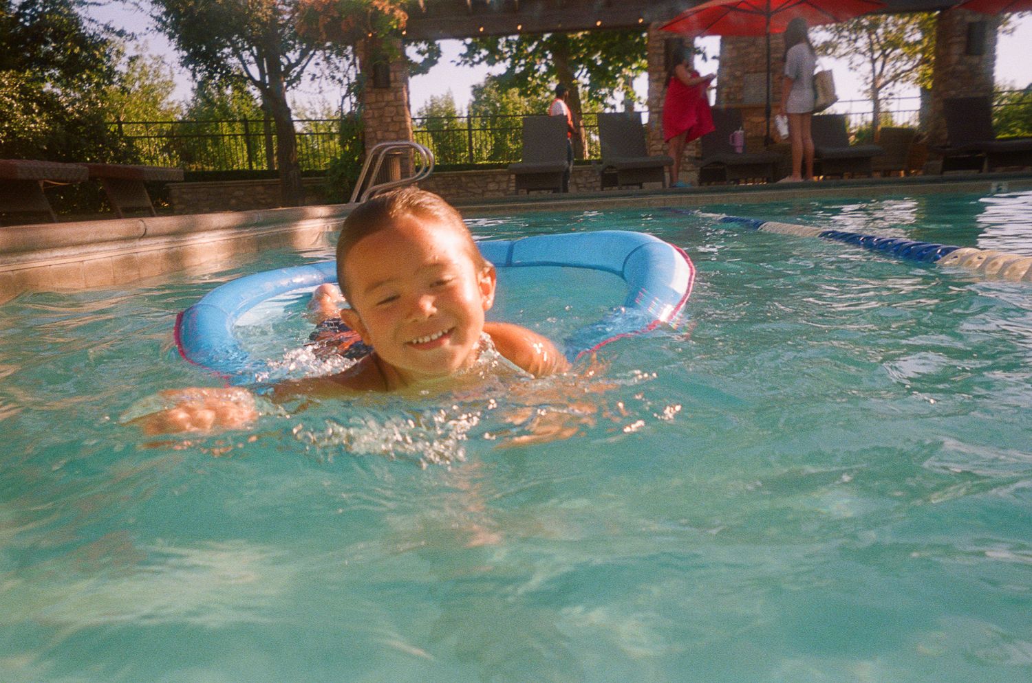 Young swimmer floating with an inflatable ring in a pool under red umbrellas.