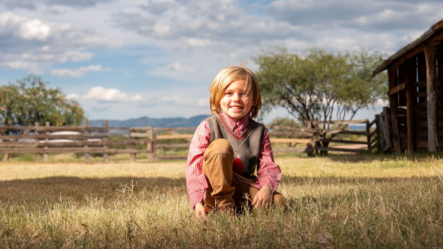 Rustic outdoor portrait in a grassy field with barn and mountains in background.