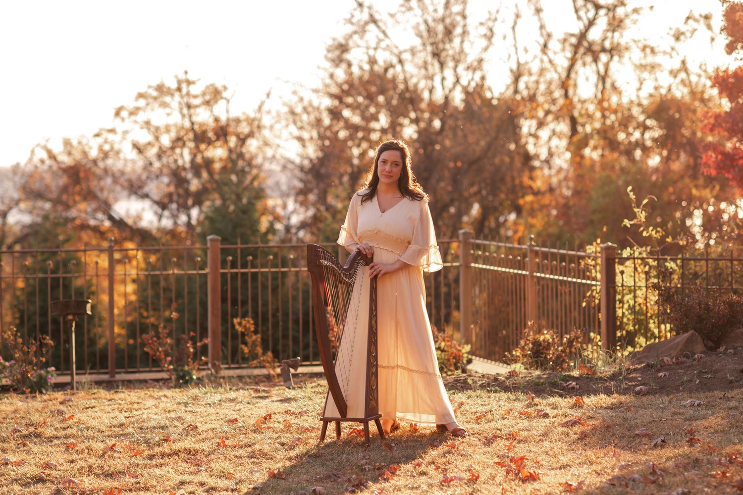 A dreamy autumn scene with a person in white standing near ornate metal railings at golden hour.