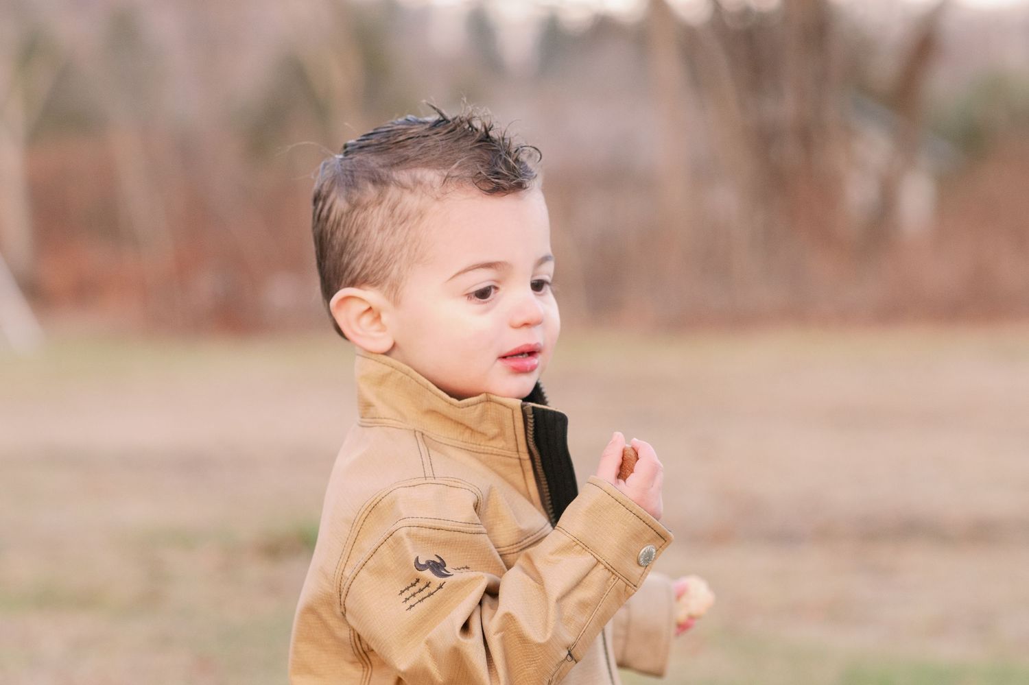 A candid outdoor portrait of a young one wearing a tan jacket.