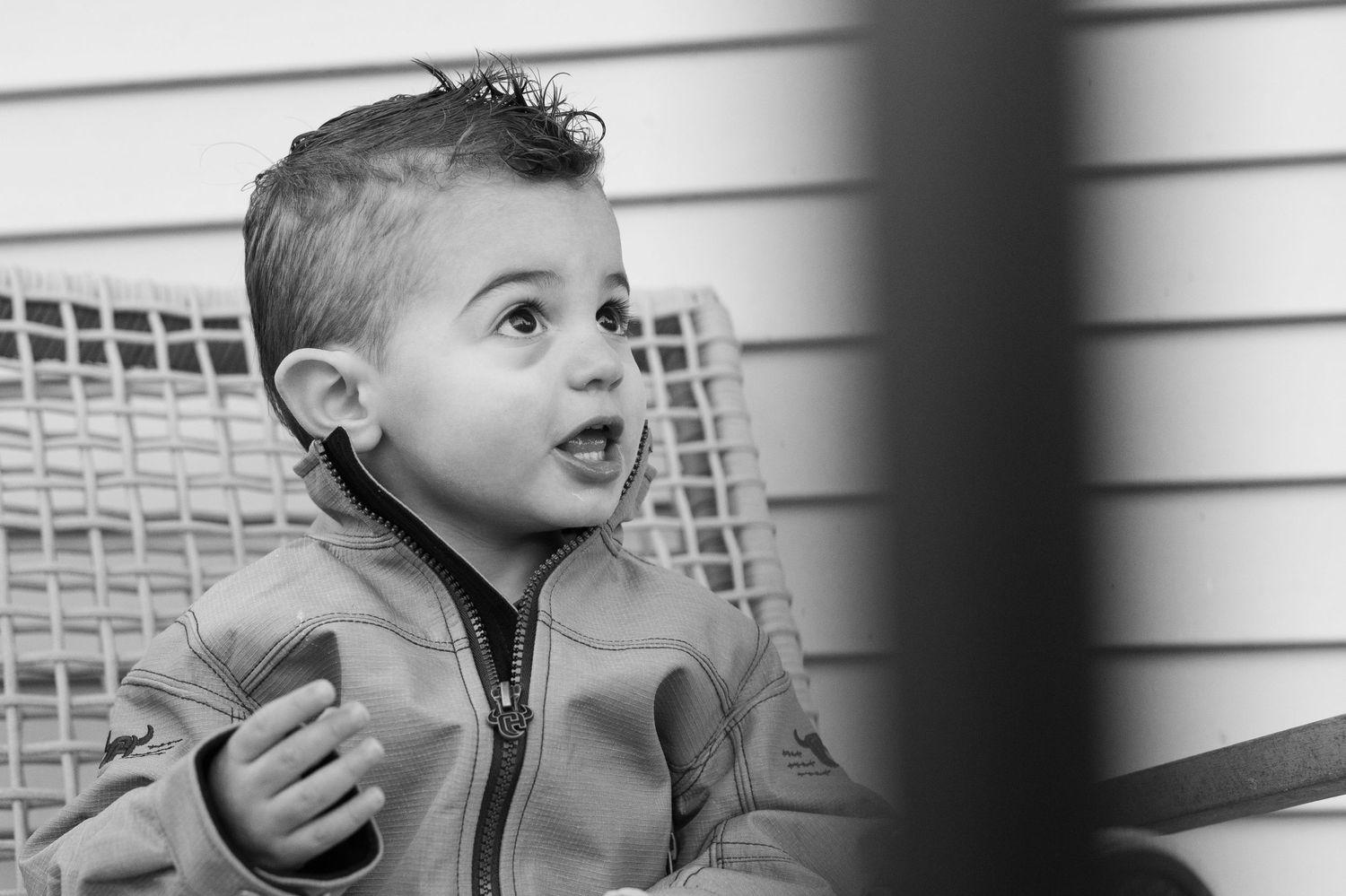 A black and white candid portrait of a young one in a jacket near a porch railing.