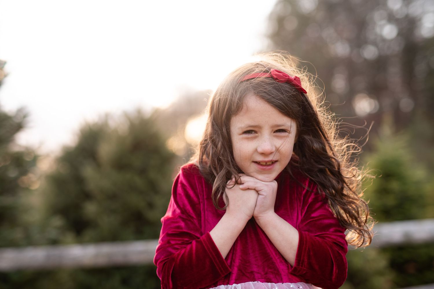 A person in a red sweater laughs while sitting outdoors with trees in the background.