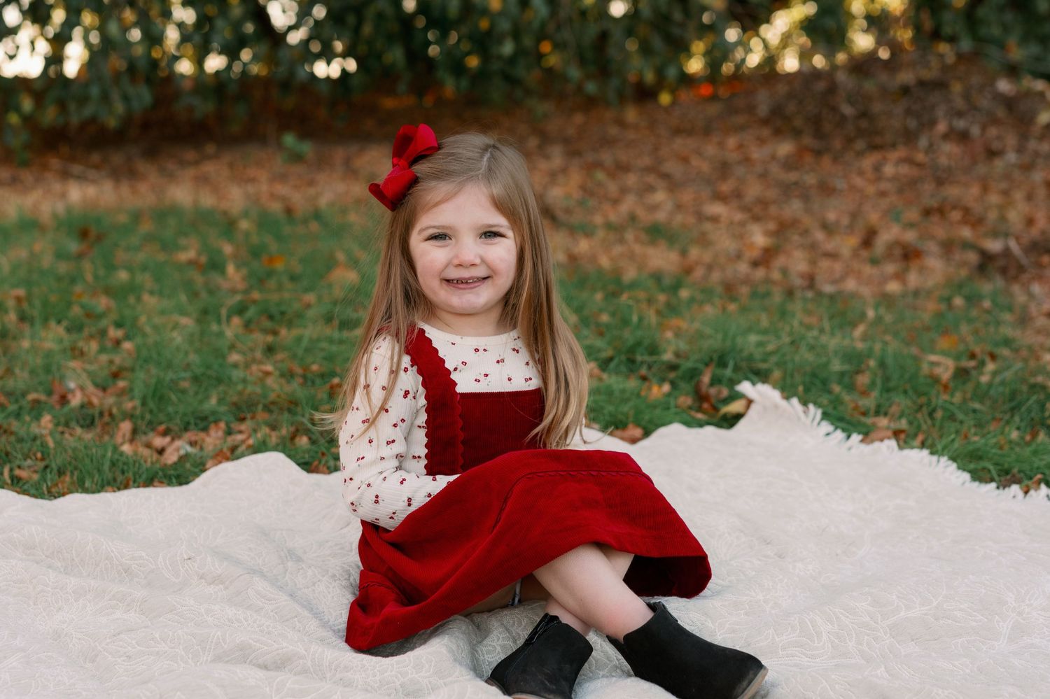 A red velvet dress and lace outfit sits elegantly on a white blanket in an autumn outdoor setting.