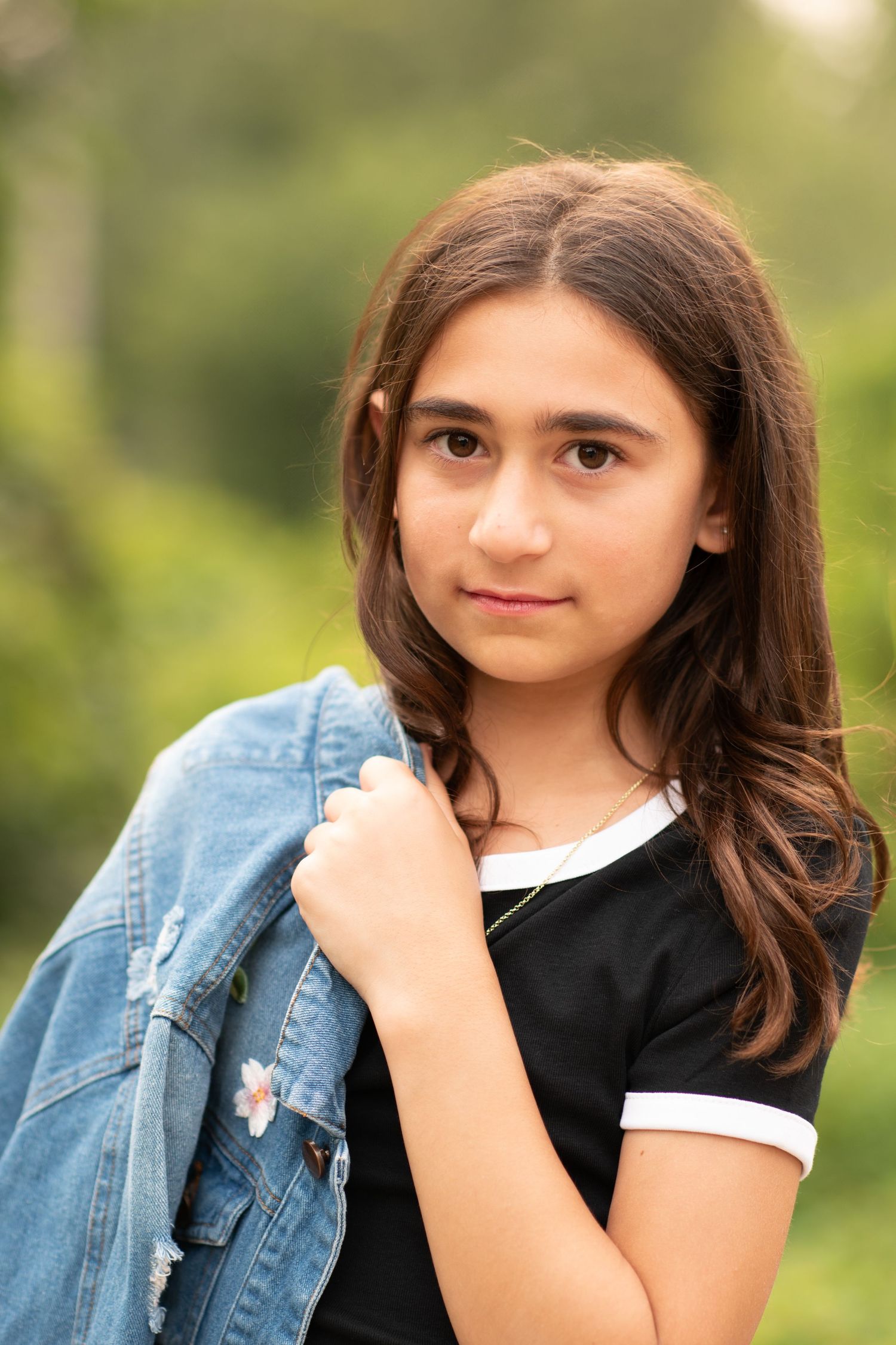 A casual outdoor portrait featuring a denim jacket and dark top against a soft natural background.
