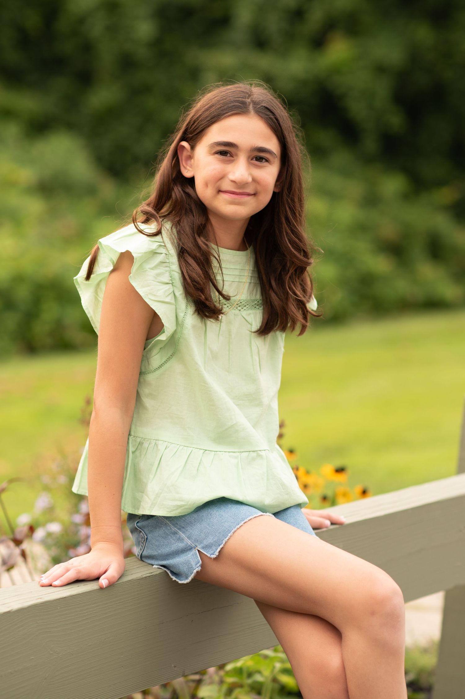 A casual summer portrait of someone sitting outdoors on a white ledge wearing denim shorts and a mint green top.