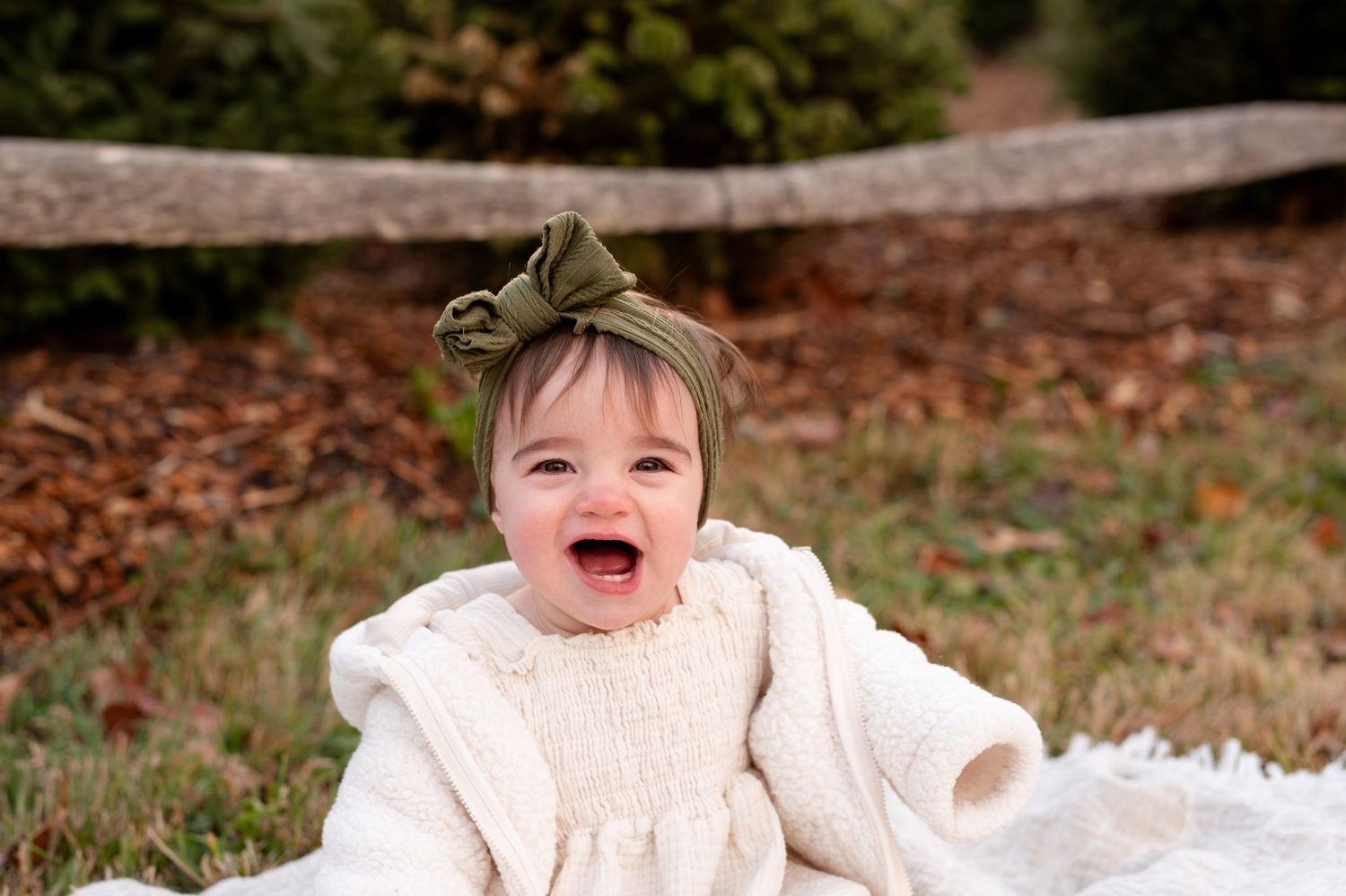 A baby wearing a white sweater laughs and plays while sitting in autumn leaves outdoors.
