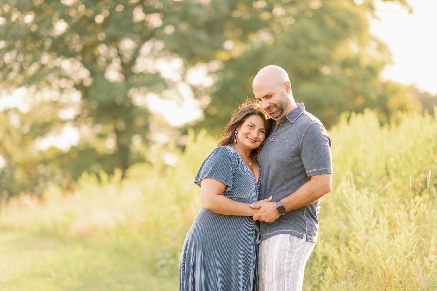 A couple embraces in a sunlit field during golden hour.