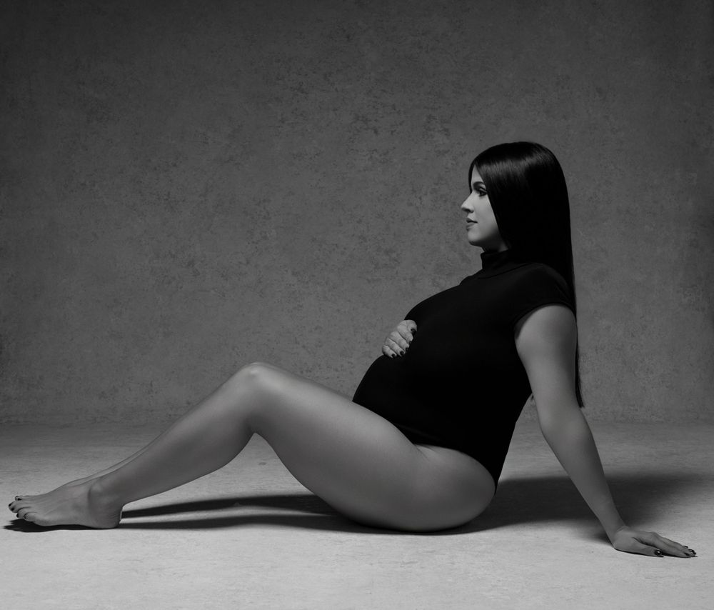 Artistic black and white studio photograph of a model in leotard reclining on floor.