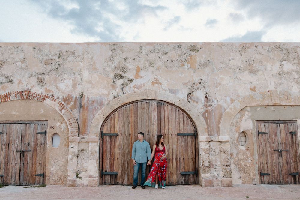 A couple poses against rustic wooden doors of an old stone building.