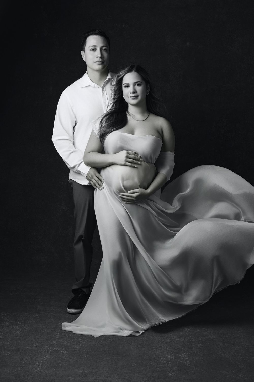 Classic black and white studio maternity portrait with flowing dress.