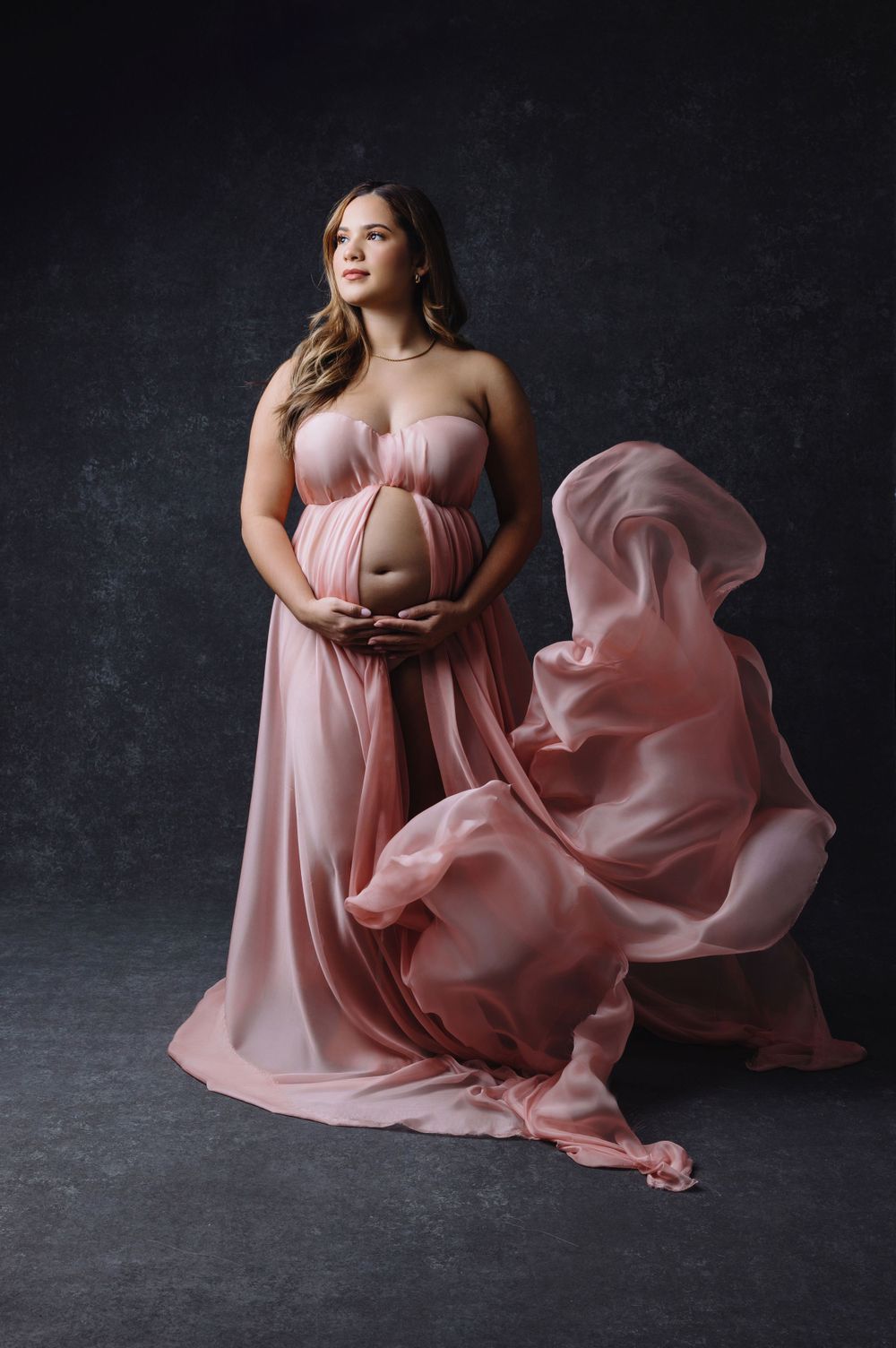 Maternity portrait in flowing pink gown with dramatic fabric movement.