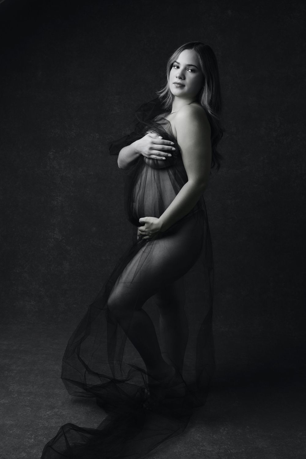 Black and white artistic maternity portrait with flowing sheer fabric.