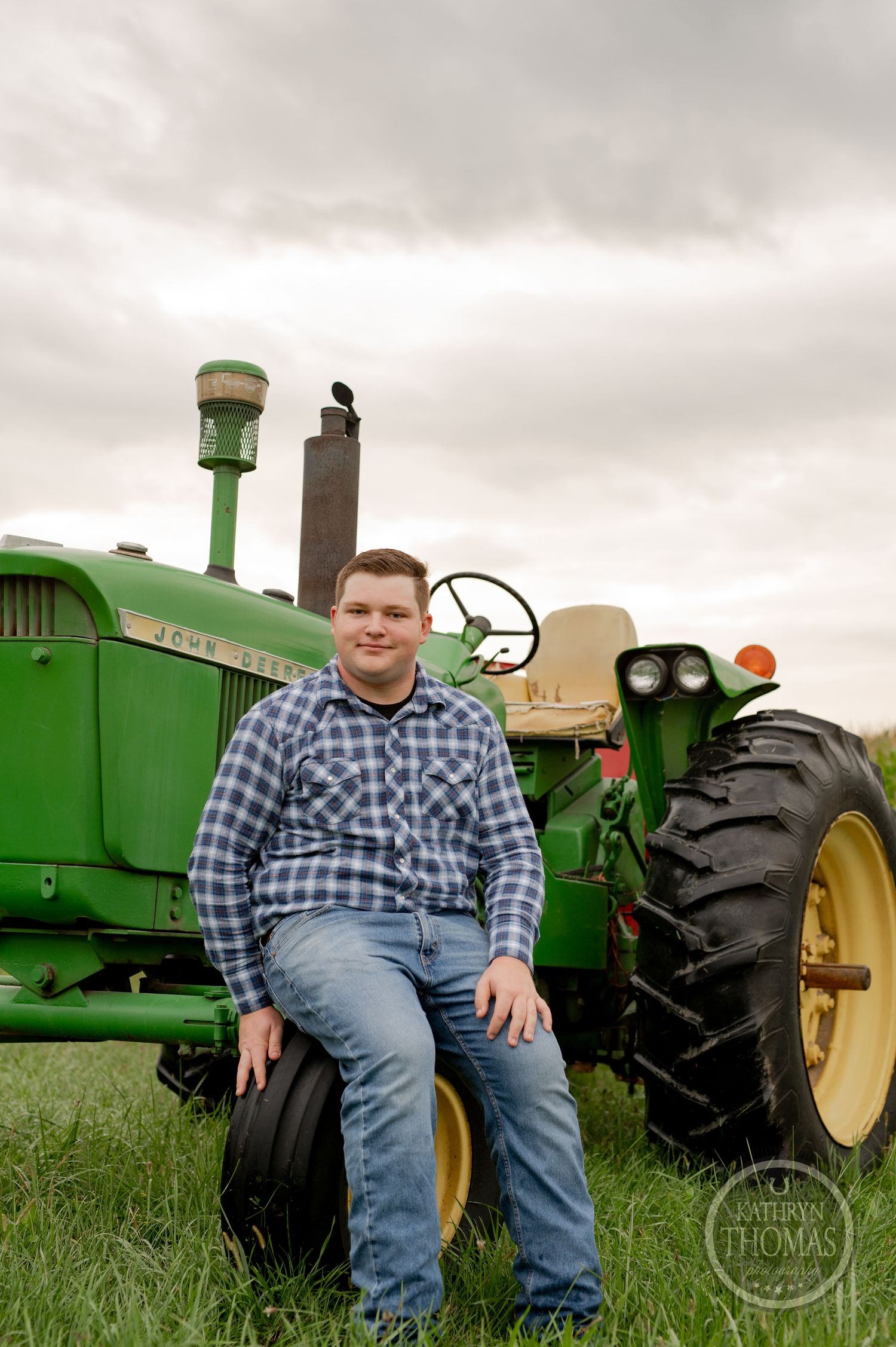 A person sits on the tire of a vintage John Deere tractor in a farm field.