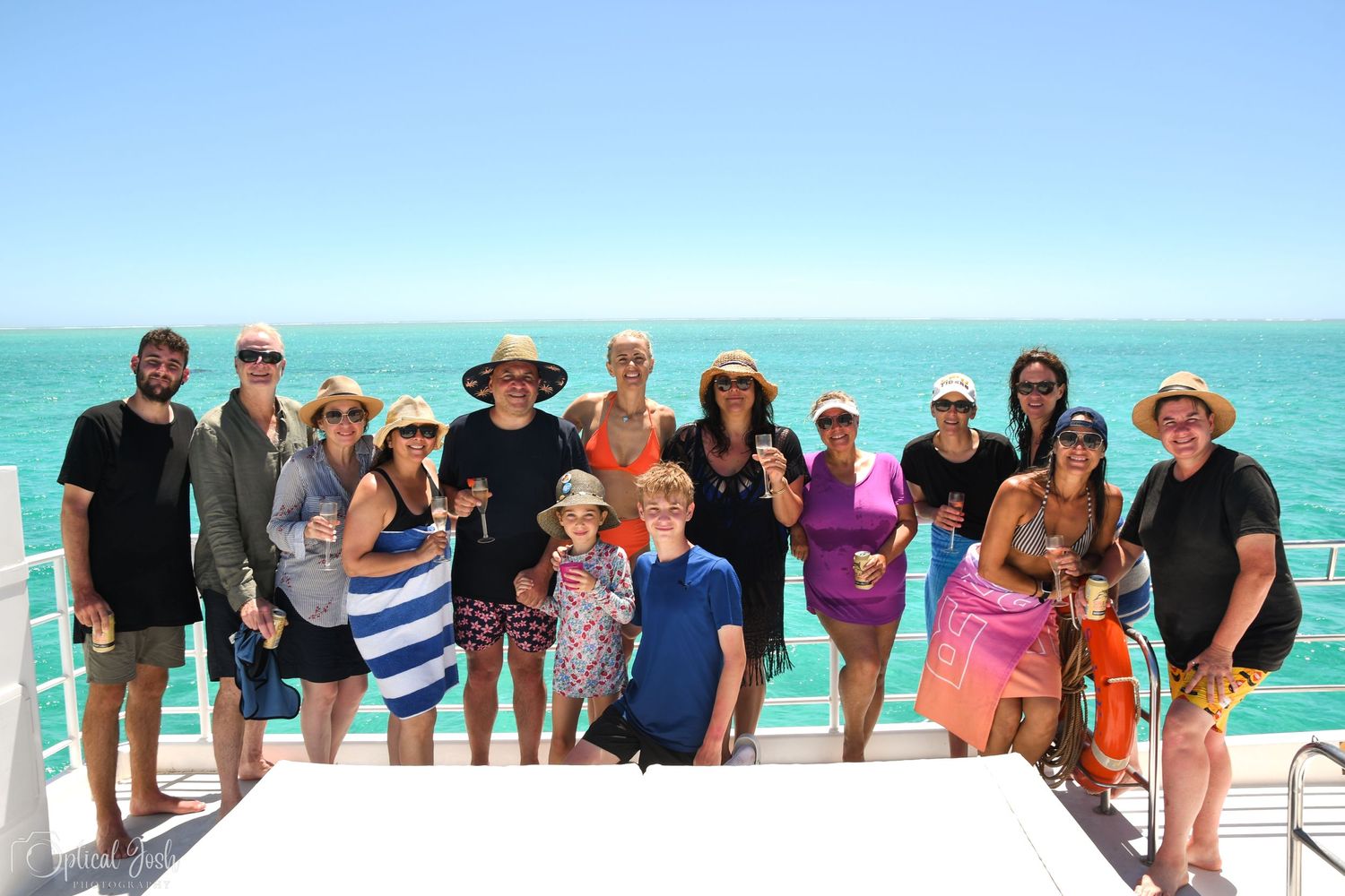 Group photo of friends enjoying a sunny day on a boat with turquoise ocean waters in the background. (Optical Josh)