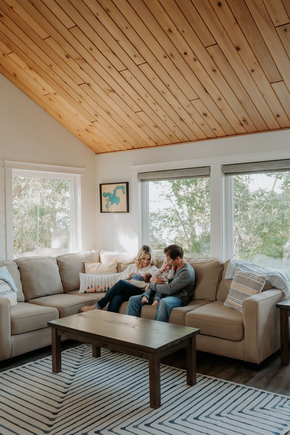 Family relaxing together in a bright living room with wood paneled ceiling and geometric rug.