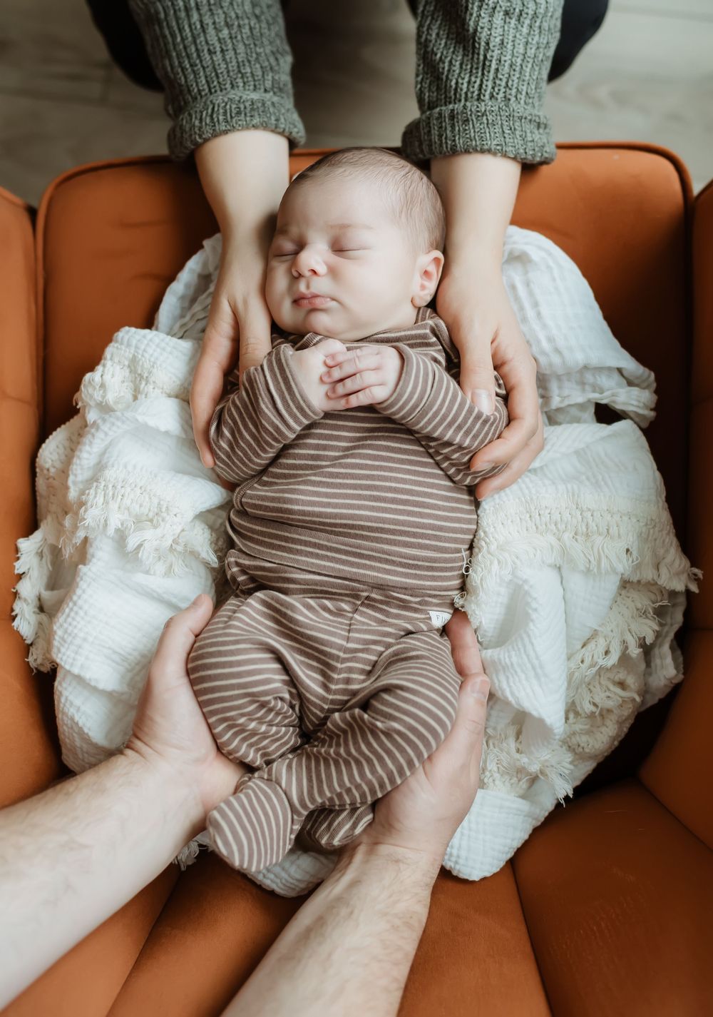 Newborn rests peacefully on a brown leather couch wearing striped sleepwear.