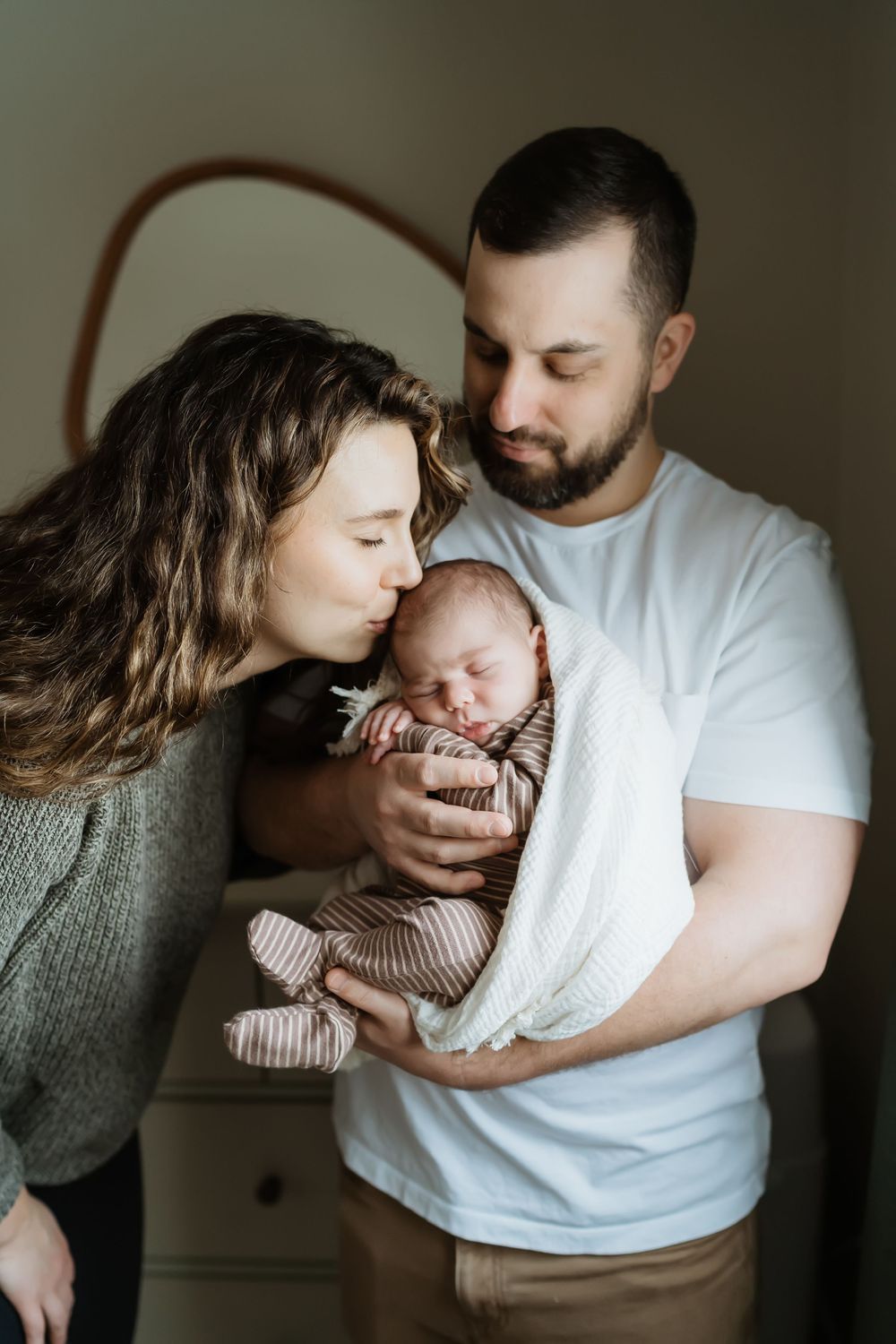 Intimate lifestyle photograph of parents embracing their newborn in a darkly lit room.