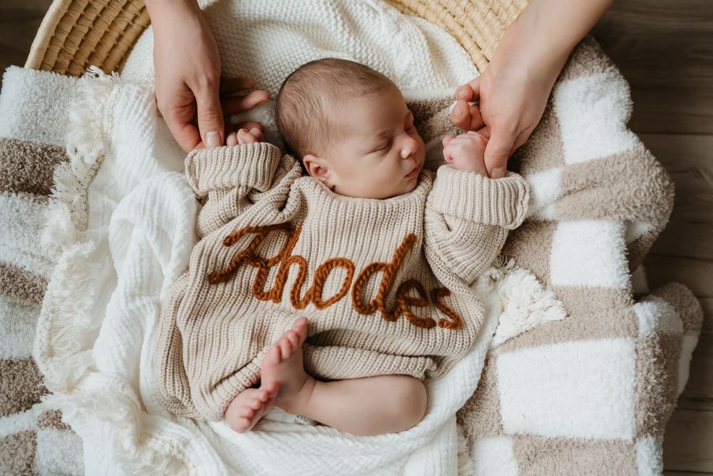 Newborn lying on soft white knitted blanket wearing neutral colored clothing.