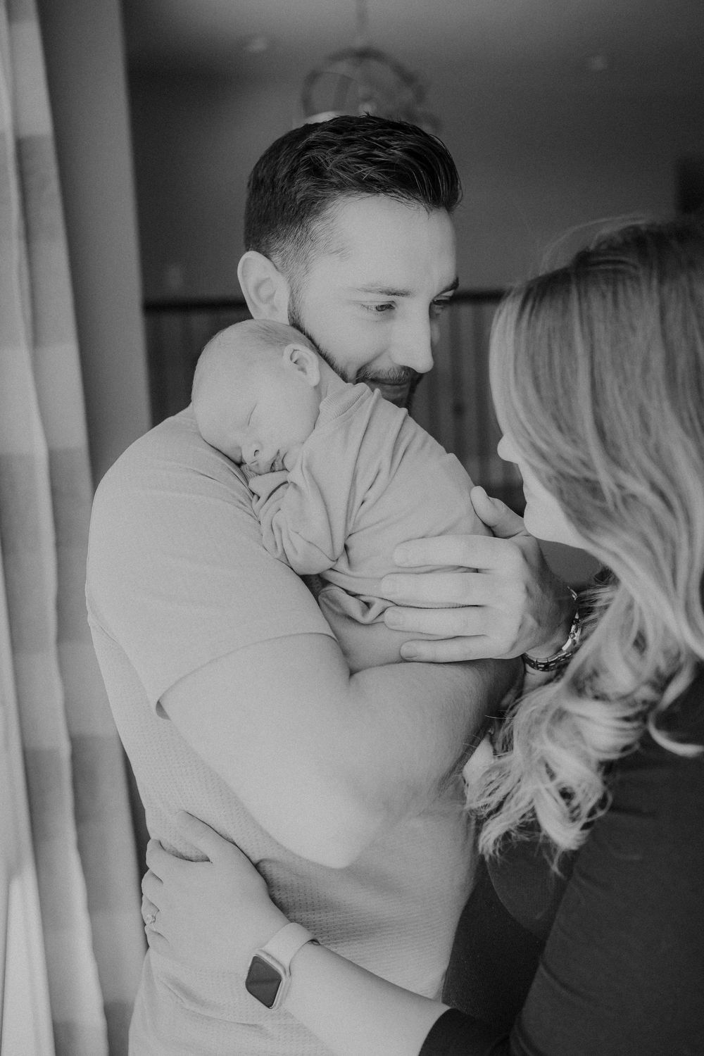 Black and white intimate portrait of family with newborn baby in home setting.