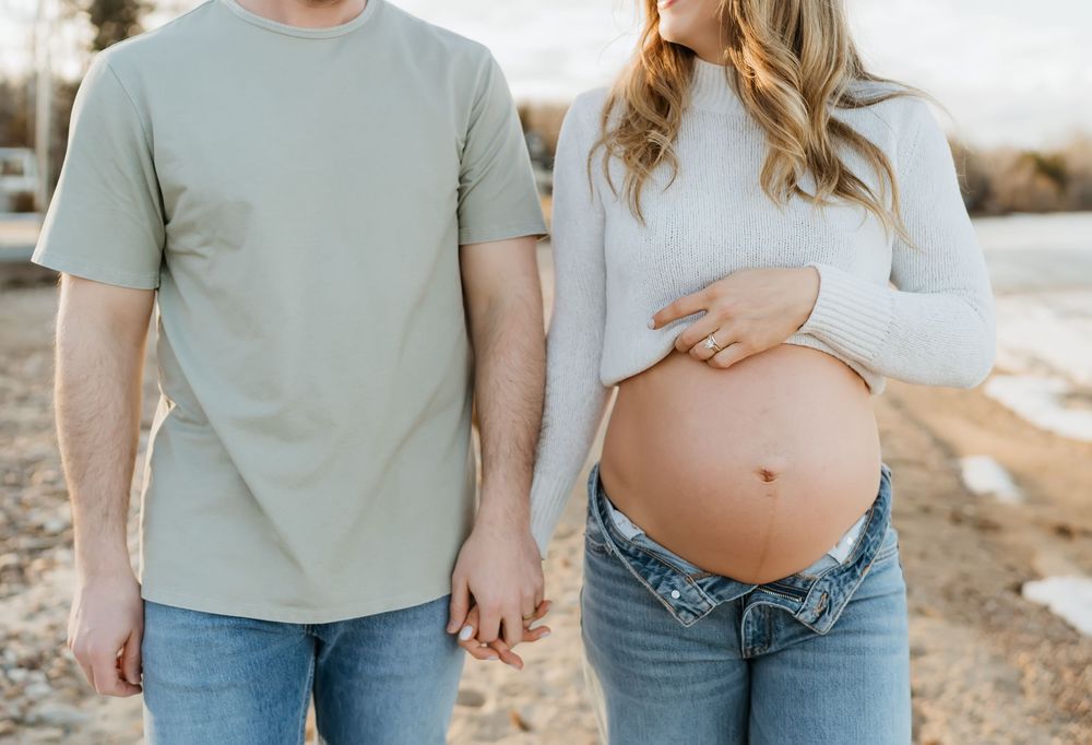 Couple in casual wear embracing during outdoor maternity photo session at golden hour.