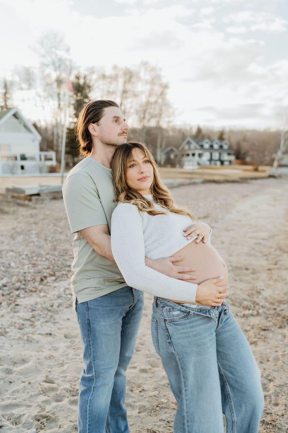 Romantic maternity photos of couple in coordinated outfits sharing intimate moments on beach.