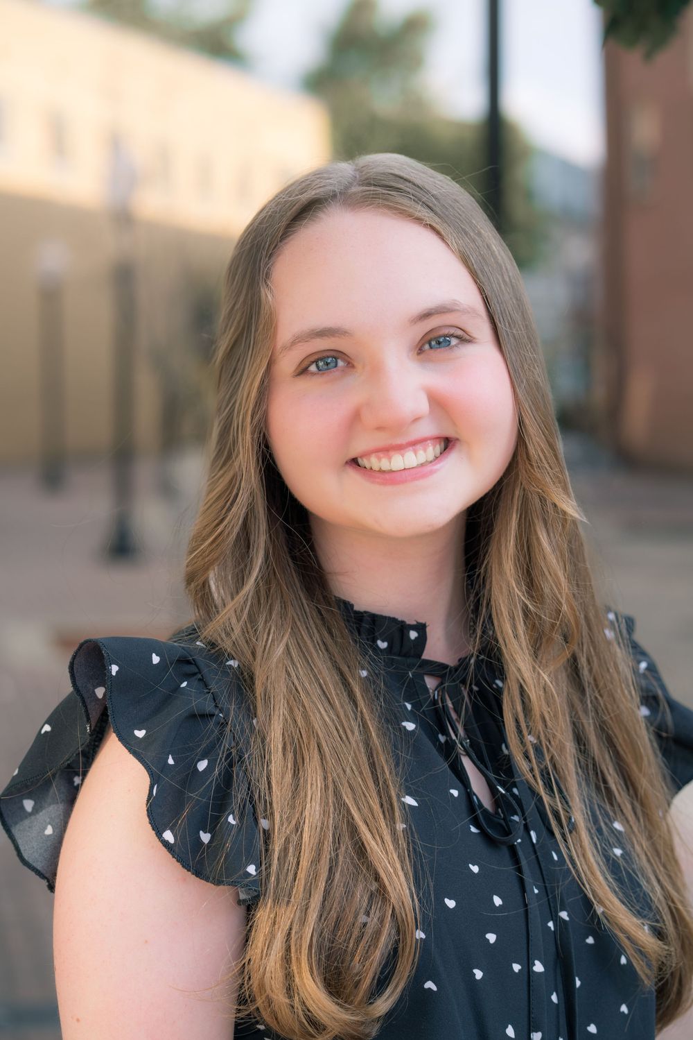 Outdoor portrait of someone wearing a black polka dot top with long brown hair.