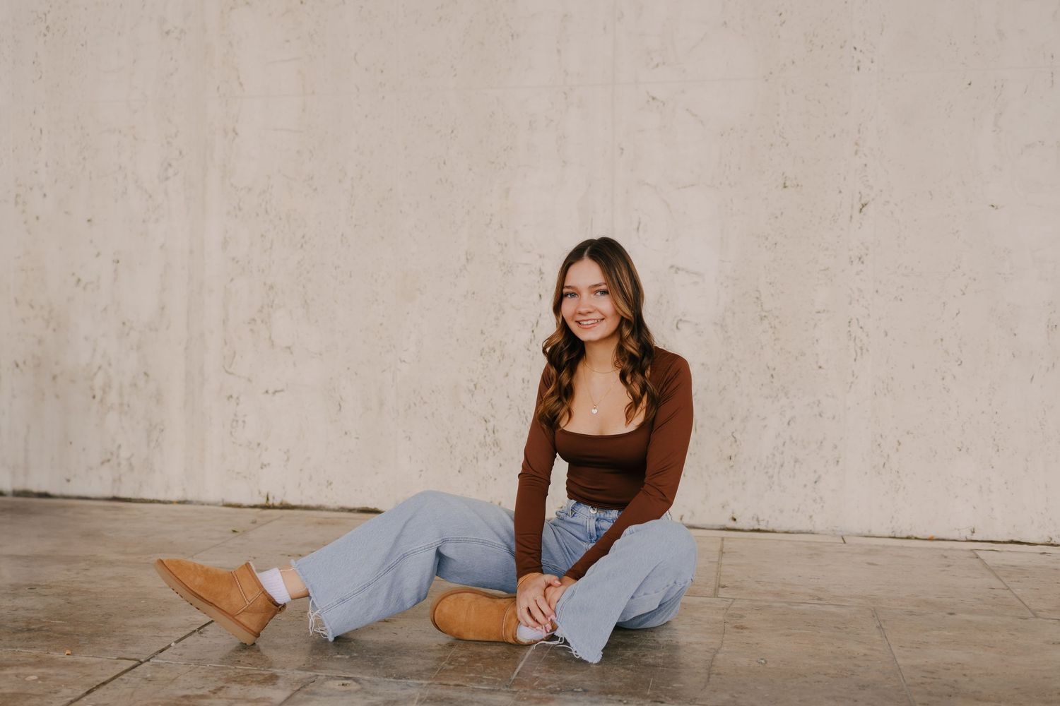 Graduate in cap and gown posing under classical columns on campus.