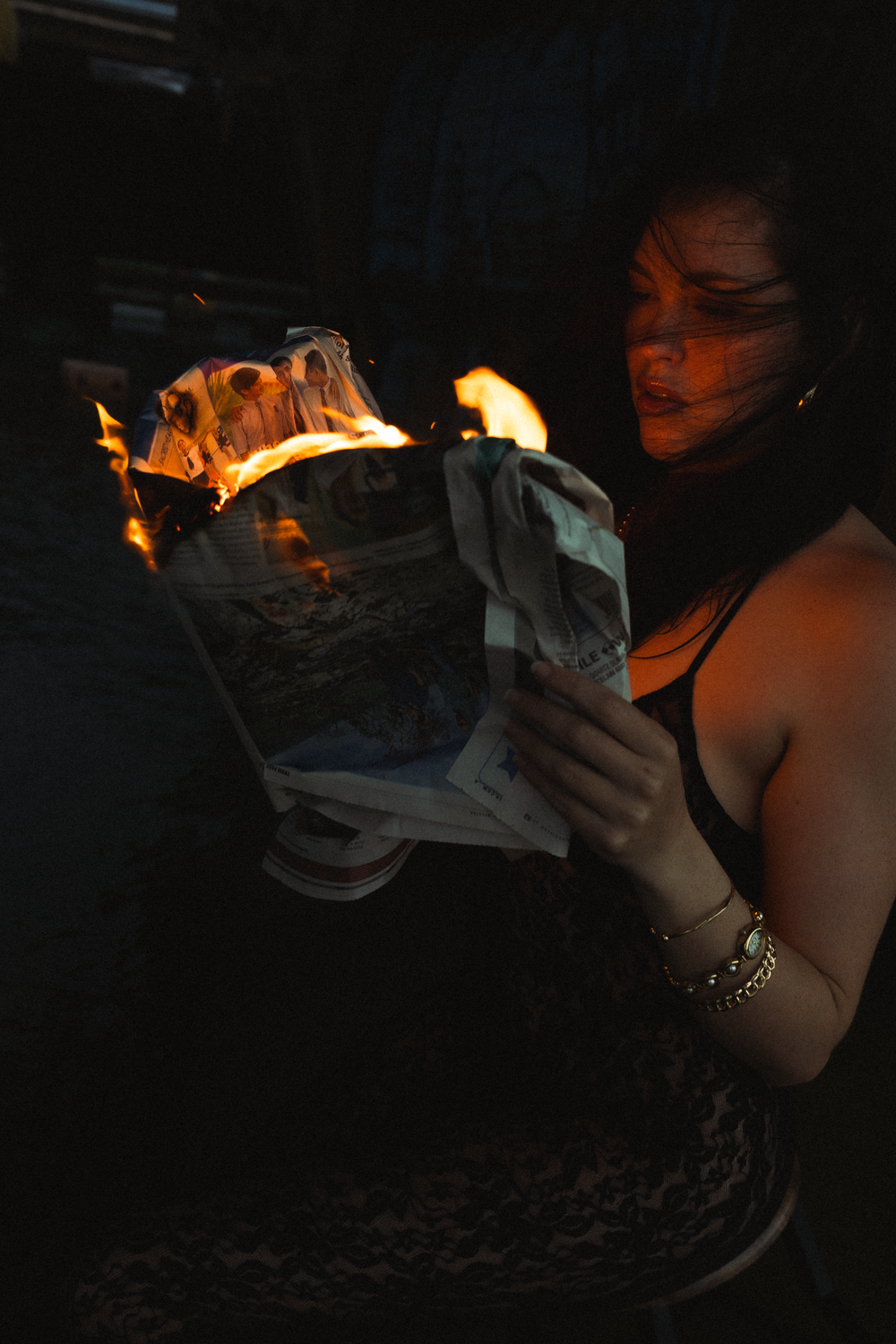 Moody nighttime scene with paper being burned, creating dramatic orange flames in darkness.