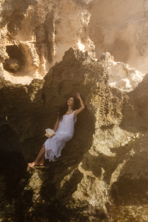 Figure in white dress posed artistically against textured cave walls in golden light.