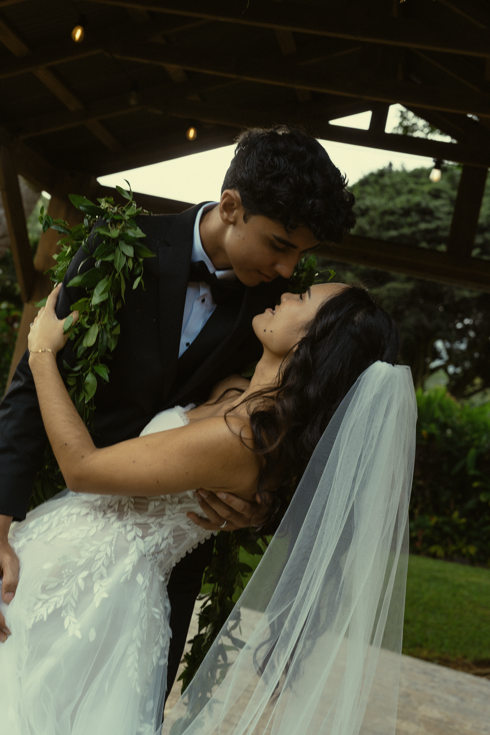 A romantic wedding couple sharing a tender kiss in an outdoor garden setting with a flowing white veil.