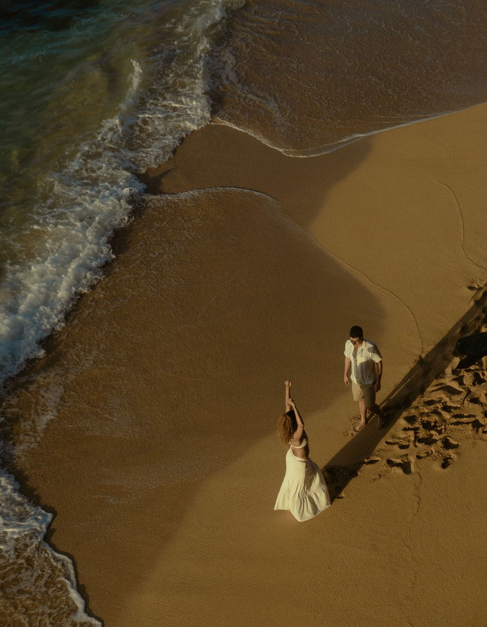 A sequence of aerial beach photos shows someone in a white dress walking along the sandy shoreline next to ocean waves.