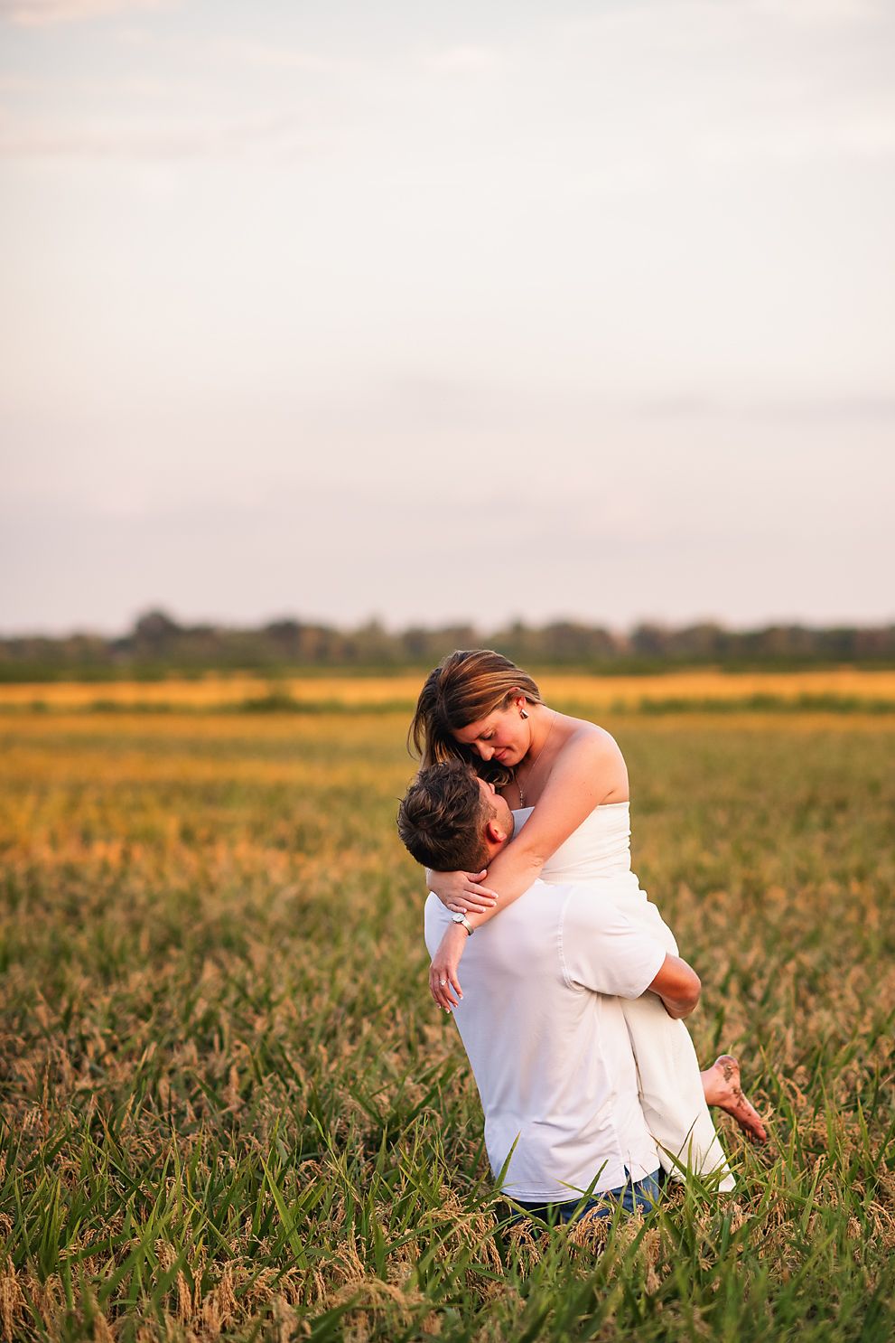 Romantic couple embracing in a golden field at sunset, man lifting woman.