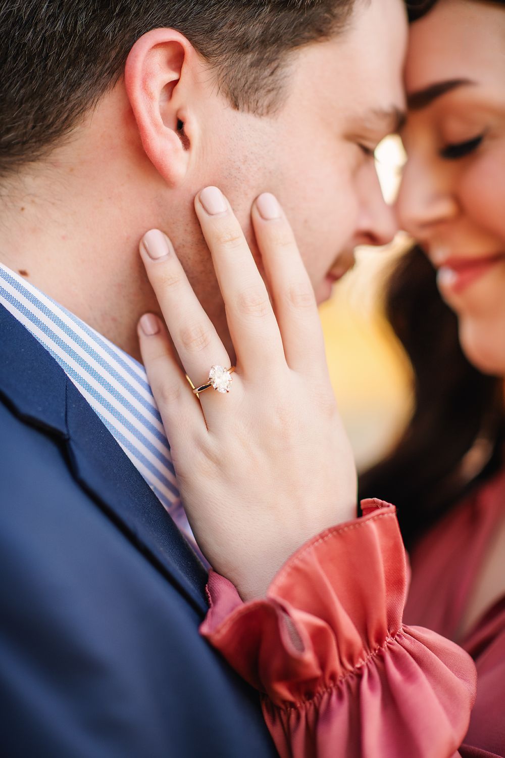 Close-up of an engaged couple touching foreheads, womans hand showing a gold diamond engagement ring.
