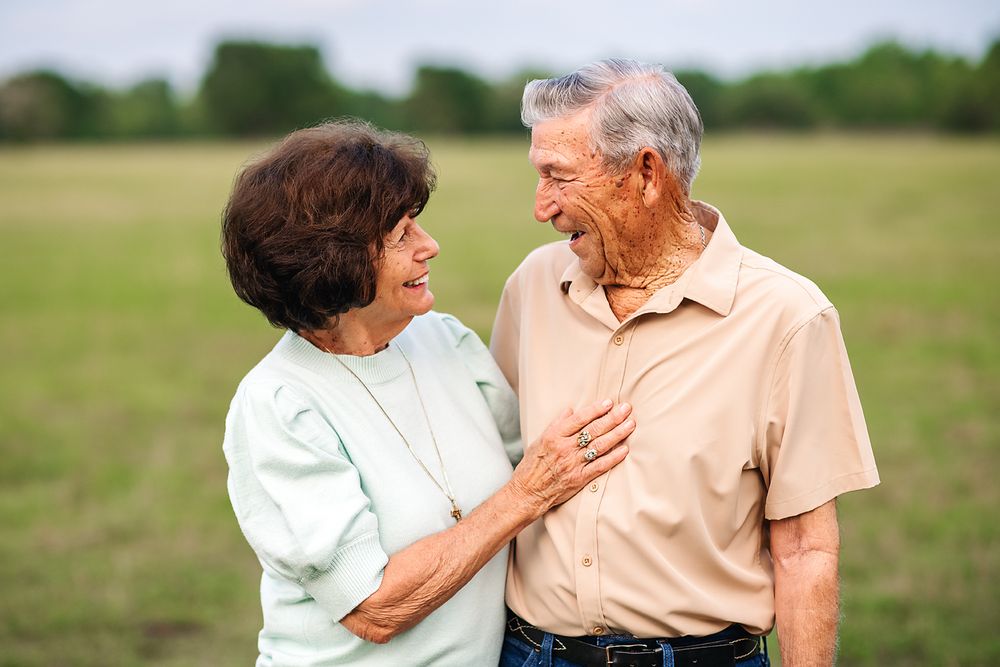 Happy elderly couple smiling and laughing together in a green field on a sunny day.